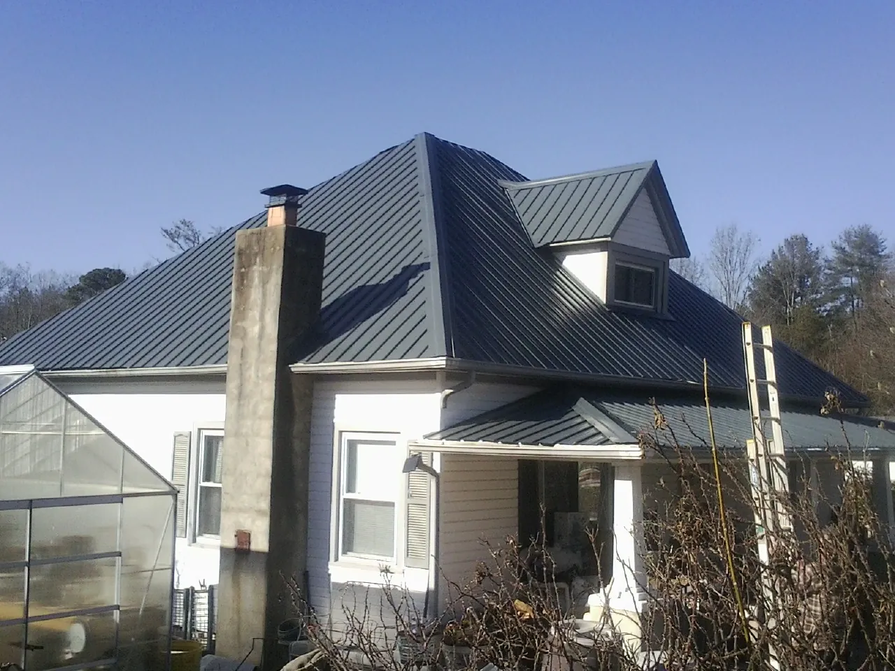 Dark blue standing seam metal roof on a white farmhouse with dormer — Slate & Tile Roof Repair by Roofing Brothers in Amery