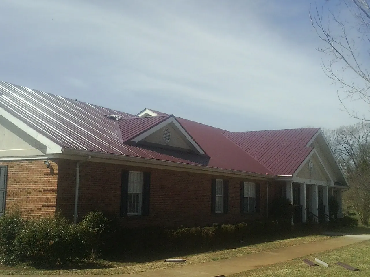 Red metal roof with gabled entries on a long brick building, from a Hail Damage Roof Repair job in Amery
