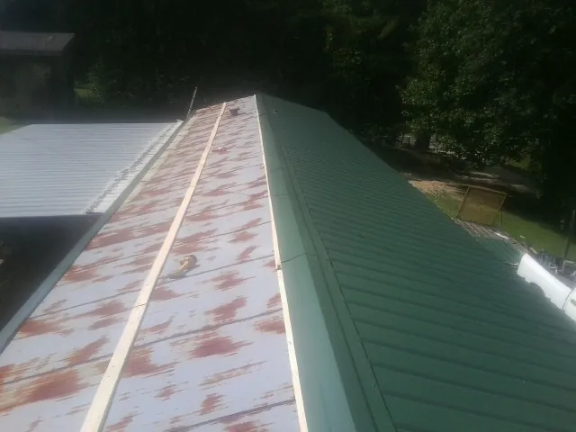 Old rusted panels beside newly installed green metal roofing — Wind Damage Roof Repair by Roofing Brothers in Amery