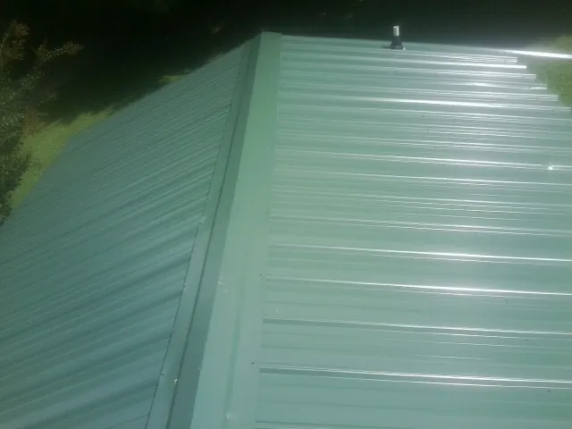 New green metal panels meeting at the ridge of a roof — Flat Roof Repair work by our crew in Amery
