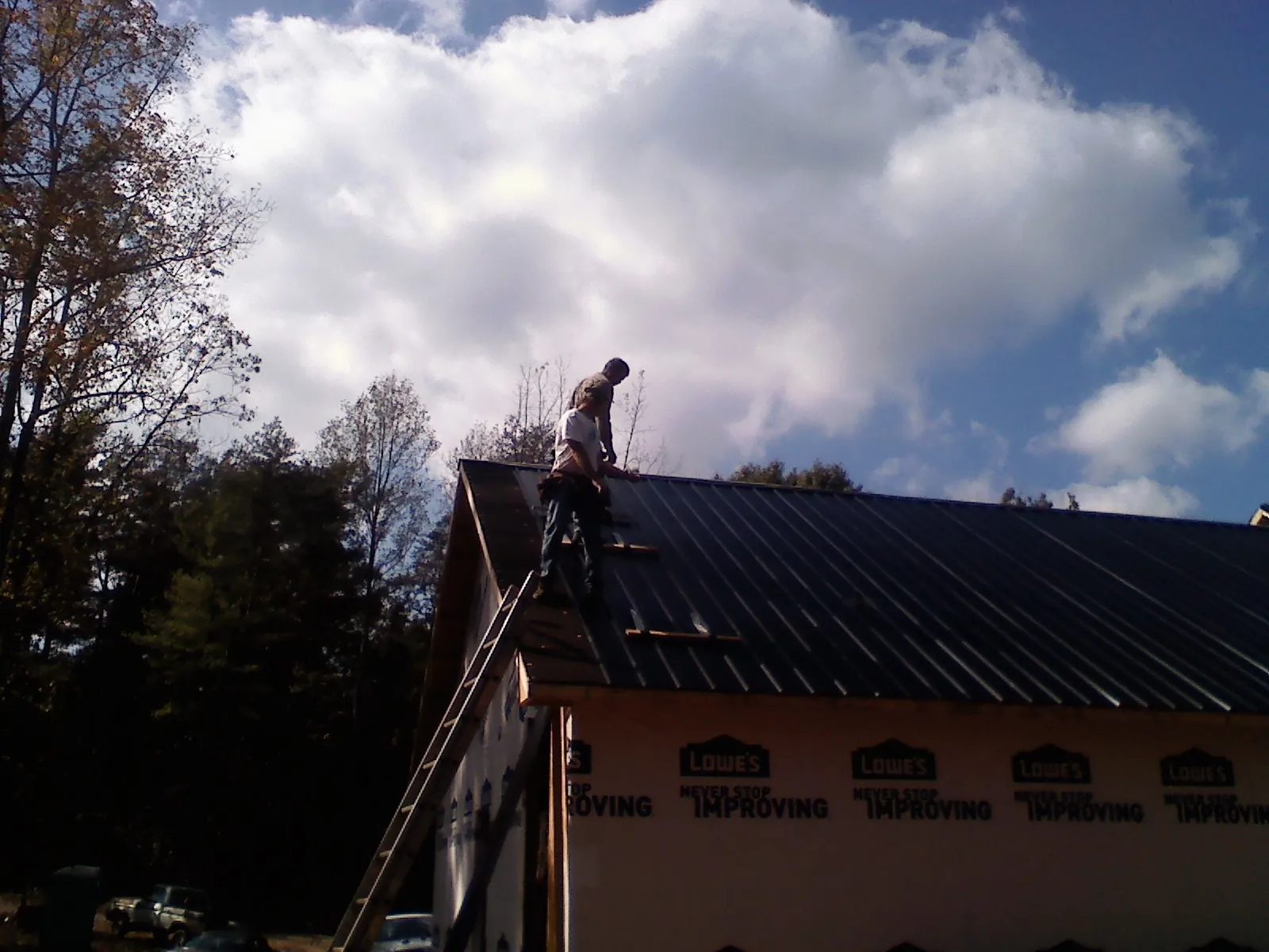 Roofer fastening dark metal panels high against a cloudy sky, from a Roof Inspection job in Amery