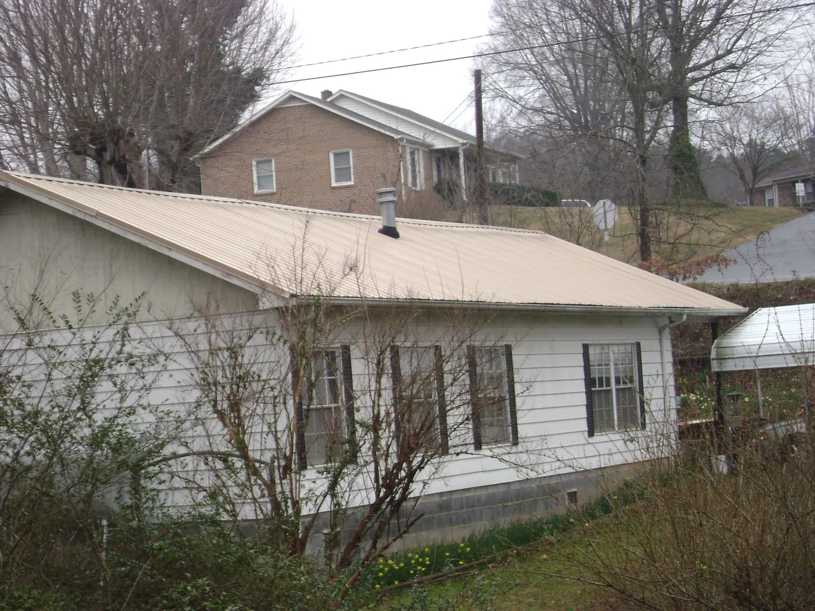Tan metal roof on a white sided house set into a hillside — Commercial Roofing by Roofing Brothers in Amery